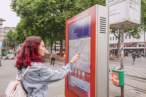 21 July 2022, Dusseldorf, Germany: Woman passenger using digital touch-screen terminal display with information about bus and train routes in the city.