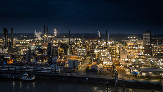 Aerial view of modern illuminated petrochemical plant at dusk with several chimneys and distillation towers. Industry with Oil Refinery, Chemical & Petrochemical plants. Tanks, distillation towers, pipes and other installations. Shot in Germany - Europe
