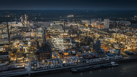 Aerial view of modern illuminated petrochemical plant at dusk with several chimneys and distillation towers. Industry with Oil Refinery, Chemical & Petrochemical plants. Tanks, distillation towers, pipes and other installations. Shot in Germany - Europe
