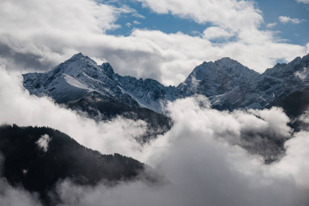 View of the snowcapped Mt. Herzogstand in the German Alps, from surface level of deep snow. Soft beams of sun break through gaps in the clouds.