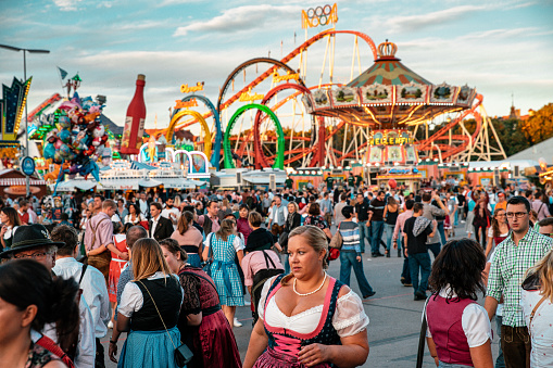 Munich, Germany - September 29, 2016: Visitors Walking Through Oktoberfest in Munich, Germany. The woman wearing typical dirndl and the men lederhosen - the traditional bavarian clothing. The Oktoberfest is the biggest beer festival of the world with over 6 million visitors each year.