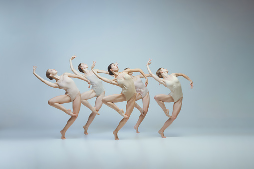 Group of young girls, ballet dancers performing, posing isolated over grey background. Flexibility, attraction, grace. Concept of art, beauty, aspiration, creativity, classic dance style, elegance