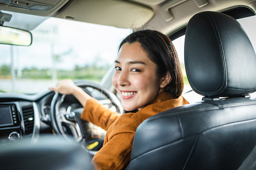 Young beautiful asian women getting new car. she very happy and excited. Smiling female driving vehicle on the road on a bright day.