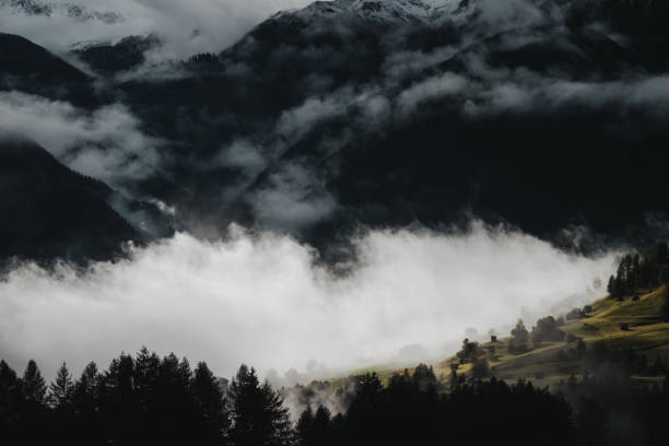 Fog and clouds move through an alpine valley with small mountain huts