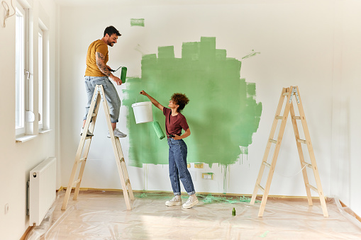Young happy couple cooperating while painting their walls during home renovation process. Copy space.