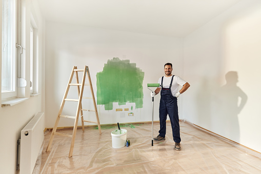 Happy male worker painting the wall in green color and looking at camera. Copy space.