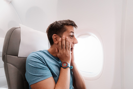 Young man is afraid to fly on an airplane and emotionally screams in fear. Panic attack and aerophobia. Accident during flight