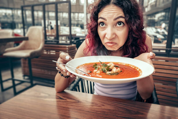 A woman dissatisfied customer of the restaurant sniffs the disgusting smell of a bowl of soup with spoiled ingredients and is going to complain to the chef A woman dissatisfied customer of the restaurant sniffs the disgusting smell of a bowl of soup with spoiled ingredients and is going to complain to the chef awful taste stock pictures, royalty-free photos & images