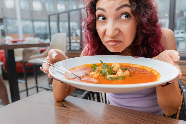 A woman dissatisfied customer of the restaurant sniffs the disgusting smell of a bowl of soup with spoiled ingredients and is going to complain to the chef A woman dissatisfied customer of the restaurant sniffs the disgusting smell of a bowl of soup with spoiled ingredients and is going to complain to the chef ugly soup stock pictures, royalty-free photos & images