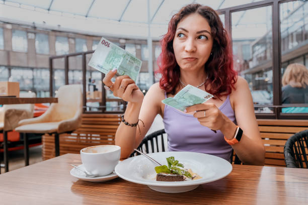 una chica frustrada paga su postre en una cafetería con un billete de euro. el concepto de inflación y un fuerte aumento de los precios - dinner currency table business fotografías e imágenes de stock