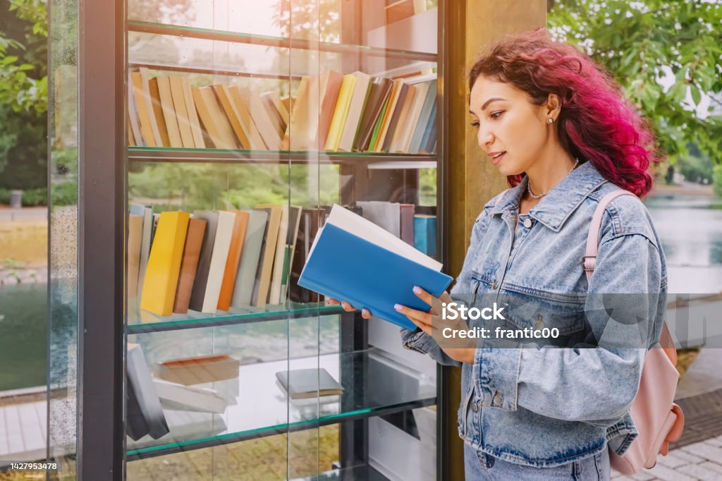 Girl choosing books at free open public library at city park for book sharing among readers. Book Stock Photo