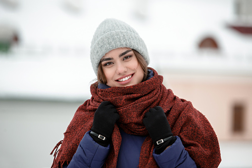 Portrait of a young happy woman enjoying winter wearing scarf and knitted hat. Smiling girl in a colorful shawl looking at camera.
