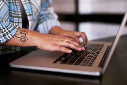 Laptop, tattoo and hands typing, a creative employee or artist online. Technology, communication and web design, worker writing email. Networking, digital marketing and a woman on internet at startup