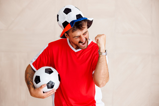 Portrait of male football fan wearing sports jersey holding cheering props celebrating his team scoring a goal at  the world championship game