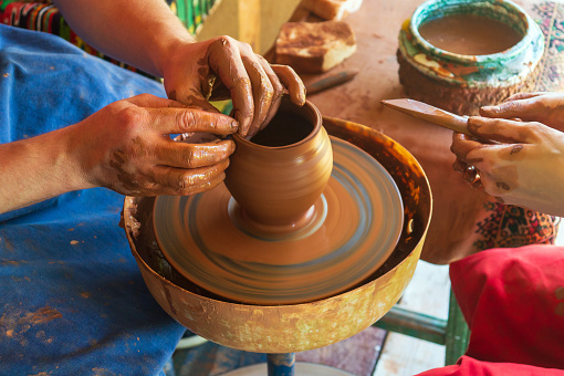 Potter makes on the pottery wheel clay pot and conducts master class. Hands of the master and child close up during work. Ancient national craft