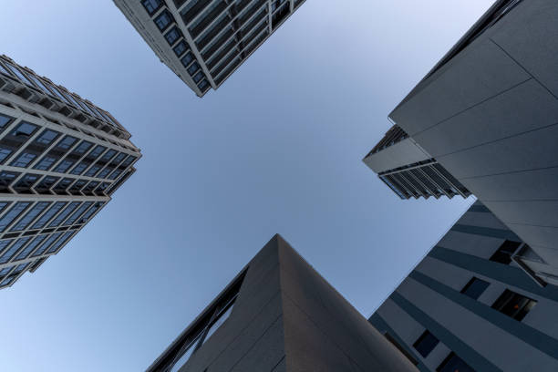 This photograph captures a dramatic upward perspective between two towering skyscrapers in New York City, creating a sense of awe and scale. The buildings’ sleek glass facades reflect light and their vertical lines converge towards the top, emphasizing their height and the city’s architectural ambition. The soft, overcast sky in the background contrasts with the sharp lines of the buildings, creating a serene yet imposing atmosphere. This image invites viewers to appreciate the modern design and the urban environment that defines New York’s skyline.