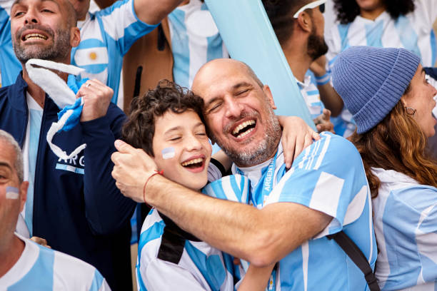 Argentinian father and son embracing each other while celebrating score at football match stock photo