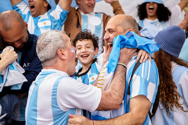 アルゼンチンのサッカーファンの友人と群衆の中に立ってゴールを祝う小さな男の子 - argentinian ethnicity 写真 ストックフォトと画像