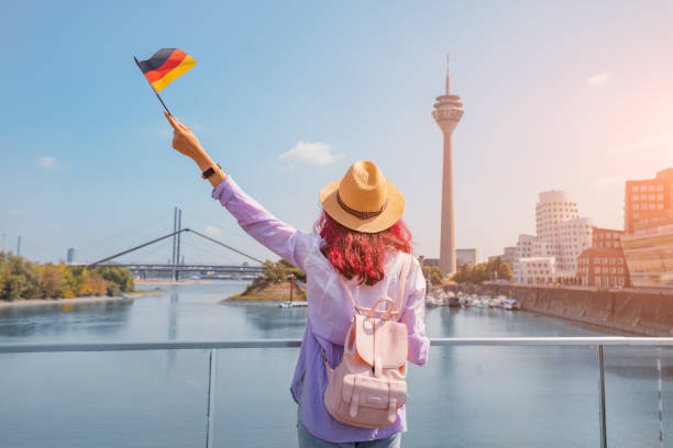 una joven asiática feliz con una bandera alemana posa en el media harbor y la torre de televisión en dusseldorf. estudiar idiomas en el extranjero y concepto de viaje - nordrhein westfalen flag fotografías e imágenes de stock