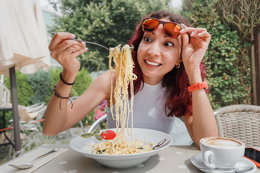 Surprised and funny asian girl eating delicious freshly cooked and hot long pasta noodles. Cafe and restaurant serving authentic italian cuisine