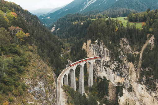 view from above on Landwasserviadukt railroad bridge in Switzerland with red train entering tunnel