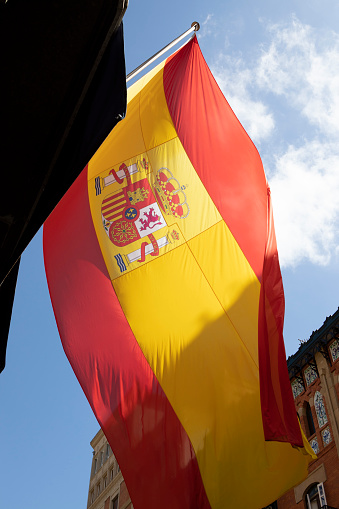 Flag of Spain with red and yellow colors waving in the wind during a sunny day with blue sky on summer