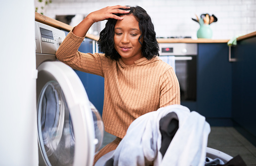 Laundry, house work and a tired woman in kitchen taking clothes out of washing machine. Stress, cleaning and a frustrated lady on the floor. Overworked, lonely and a depressed housewife busy at home
