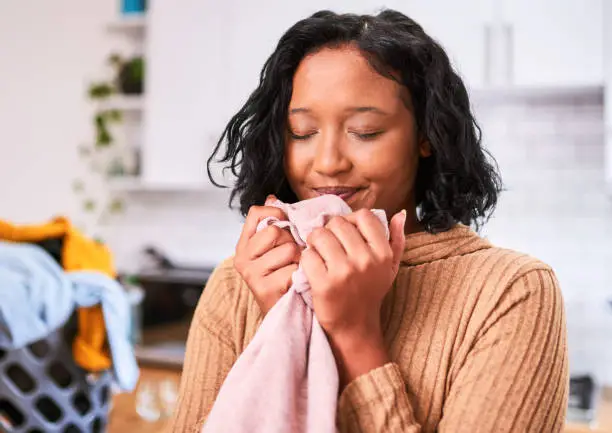 Laundry, clean clothes and woman with fabric softener, cleaning and home routine. Smell of fragrance with happy black woman cleaner and basket of clothing for hygiene, care and housewife lifestyle