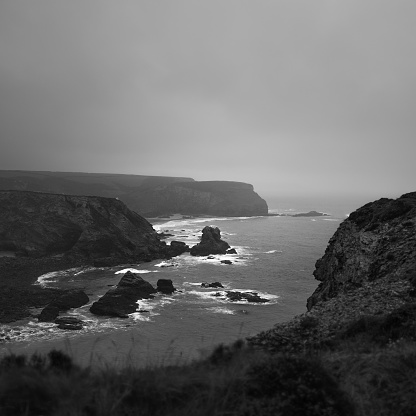 A view of the jagged rocks of the Cornish coastline with the silhouettes of people on the shore