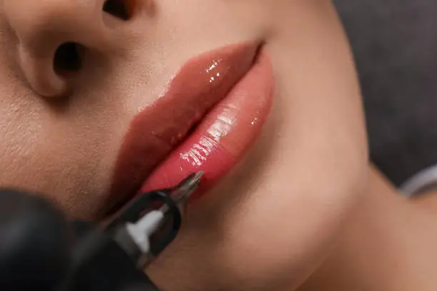 Photo of Young woman undergoing procedure of permanent lip makeup in tattoo salon, top view