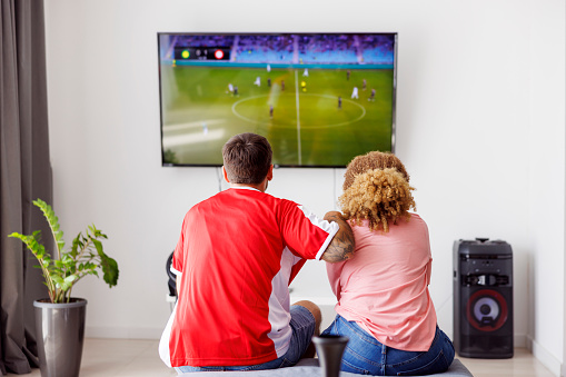 Couple having fun watching football world championship game on TV at home, cheering for their national team