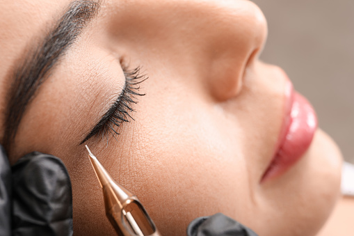 Young woman undergoing procedure of permanent eye makeup in tattoo salon, closeup