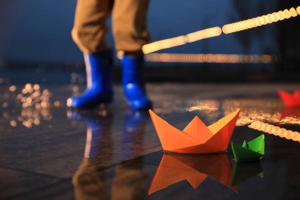 kleiner junge im freien, fokus auf papierboote in pfütze - puddle rain boot water stock-fotos und bilder