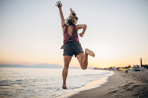 Woman jumping towards the sunset and having fun on the beach.