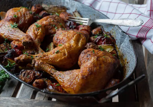 Homemade fresh cooked oven roasted chicken legs with delicious root vegetables for side dish. Served in a rustic roasting pan on wooden background
