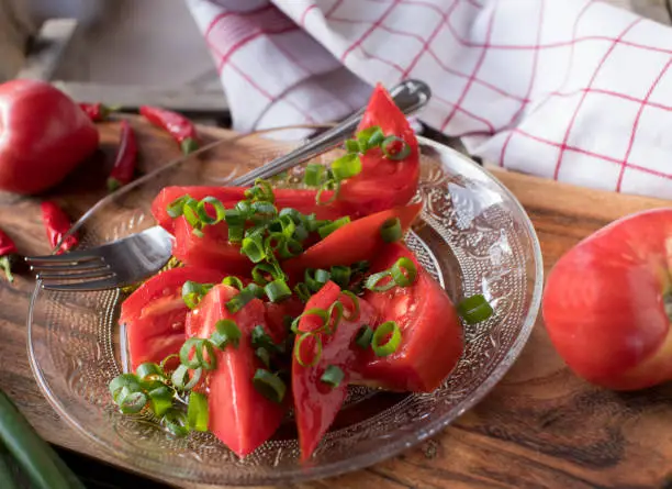 Homemade tomato salad with fresh beef tomatoes from the garden. Marinated with olive oil and chives. Served on a glass plate on wooden background