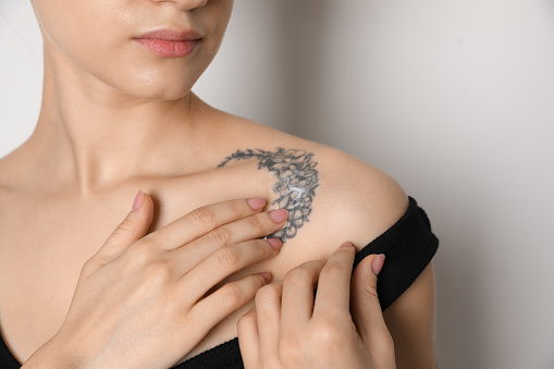 Mujer aplicando crema sobre el tatuaje en su piel contra fondo claro, primer plano photo
