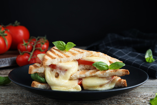 Delicious grilled sandwiches with mozzarella, tomatoes and basil on wooden table. Space for text