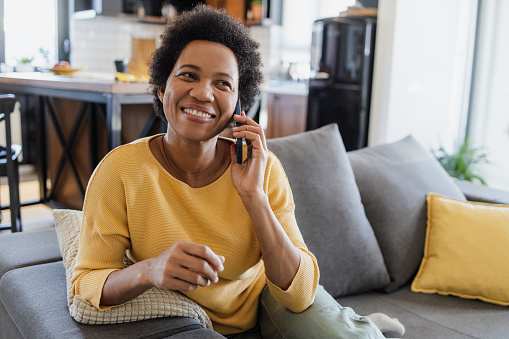 Portrait of mid adult woman sitting on the couch in the living room and talking on the phone