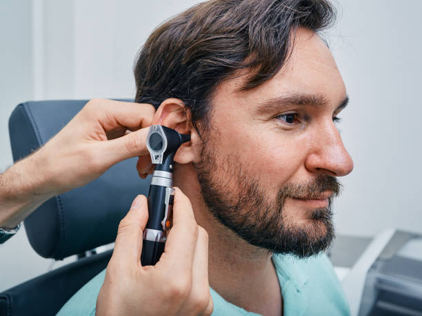 uomo adulto durante l'esame dell'orecchio presso la clinica dell'udito. audiologo che esamina l'orecchio del paziente maschio usando l'otoscopio, primo piano - esame otorino foto e immagini stock