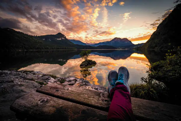Photo of Female hiker with legs on picnic table in front of a breathtaking sunset view of Altausseer See (Lake Aussee) in Ausseer Land region, Styria, Austria