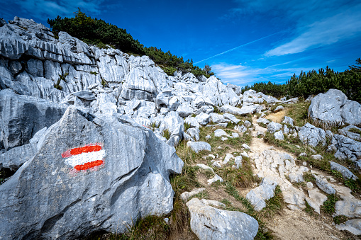 Mount Loser, Altaussee, Austria - September 6th 2022. The hiking trail on top of the Loser plateau passes some man-worked boulders, in fact, these rocks are of natural origin. In the foreground, an Austrian flag marks the way along the hiking trail towards the peak.