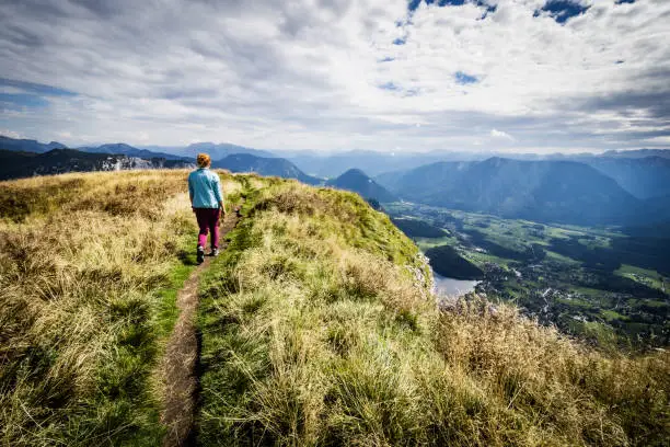 Photo of Female hiker walks along a ridge and enjoys the breathtaking view from the top of Loser mountain, Altaussee, Ausser Land, Salzkammergut, Styria, Austr