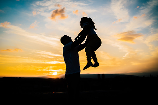 Silhouette of father and daughter in the park during sunset