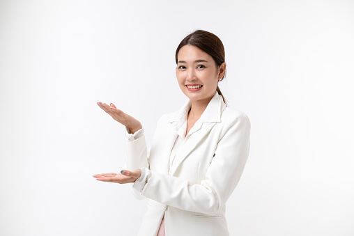 Smiling young business Asian woman in white suit pointing aside with hands open palms showing copy space . isolated on white background