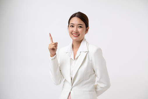 Smiling young business Asian woman in white suit pointing finger hands up to copy space . isolated on white background