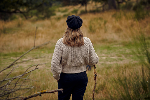 Senior woman in yellow jacket, raincoat with hood, walking along shore of lake against background of autumn landscape, colored forest. Back view of pensioner active recreation, wellness walk in nature