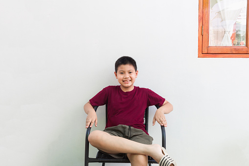 Thai Asian boy sitting in a chair smiling, looking handsome and fun on white cafe wall in holiday