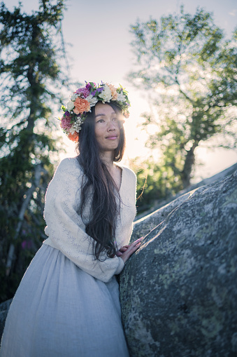 Caucasian-Chinese beautiful woman dressed in linen, fresh flower wreath, admiring the grand views of Koli National Park and Pielinen Lake in the mood of folklores