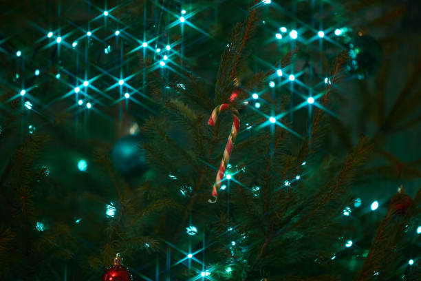 Close up of holiday electric blue garlands on fir branch with Christmas tree decoration and candy sweet. Candy cane hanging onto the branch of a Christmas tree Close up of holiday electric blue garlands on fir branch with Christmas tree decoration and candy sweet. Candy cane hanging onto the branch of a Christmas tree candy cane flash stock pictures, royalty-free photos & images